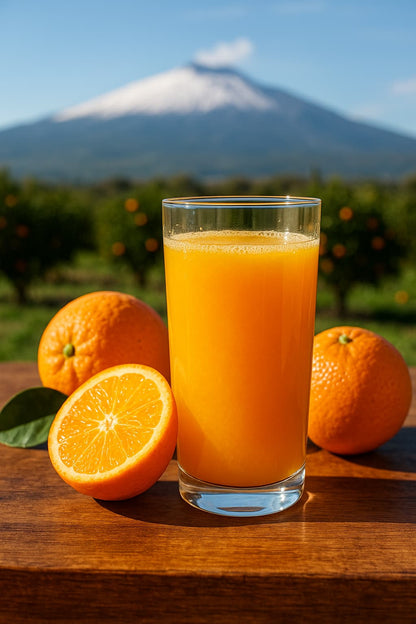 Bicchiere di spremuta fresca di arance siciliane con arance intere e Etna sullo sfondo.